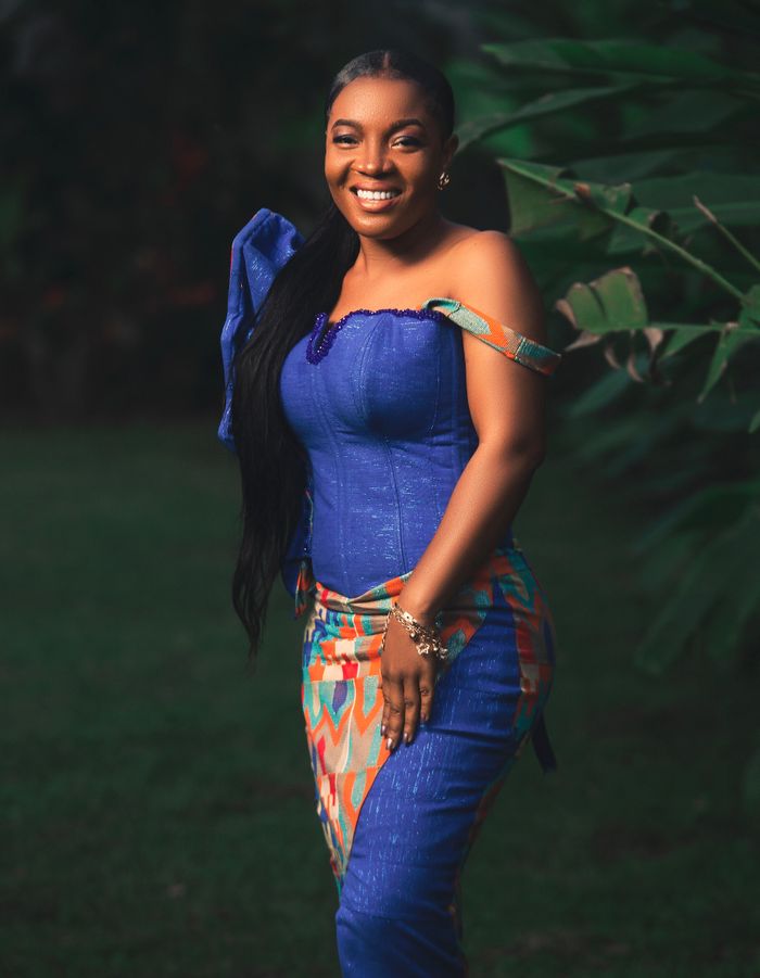 Portrait of a smiling woman in traditional Ghanaian attire, outdoors in Akropong.