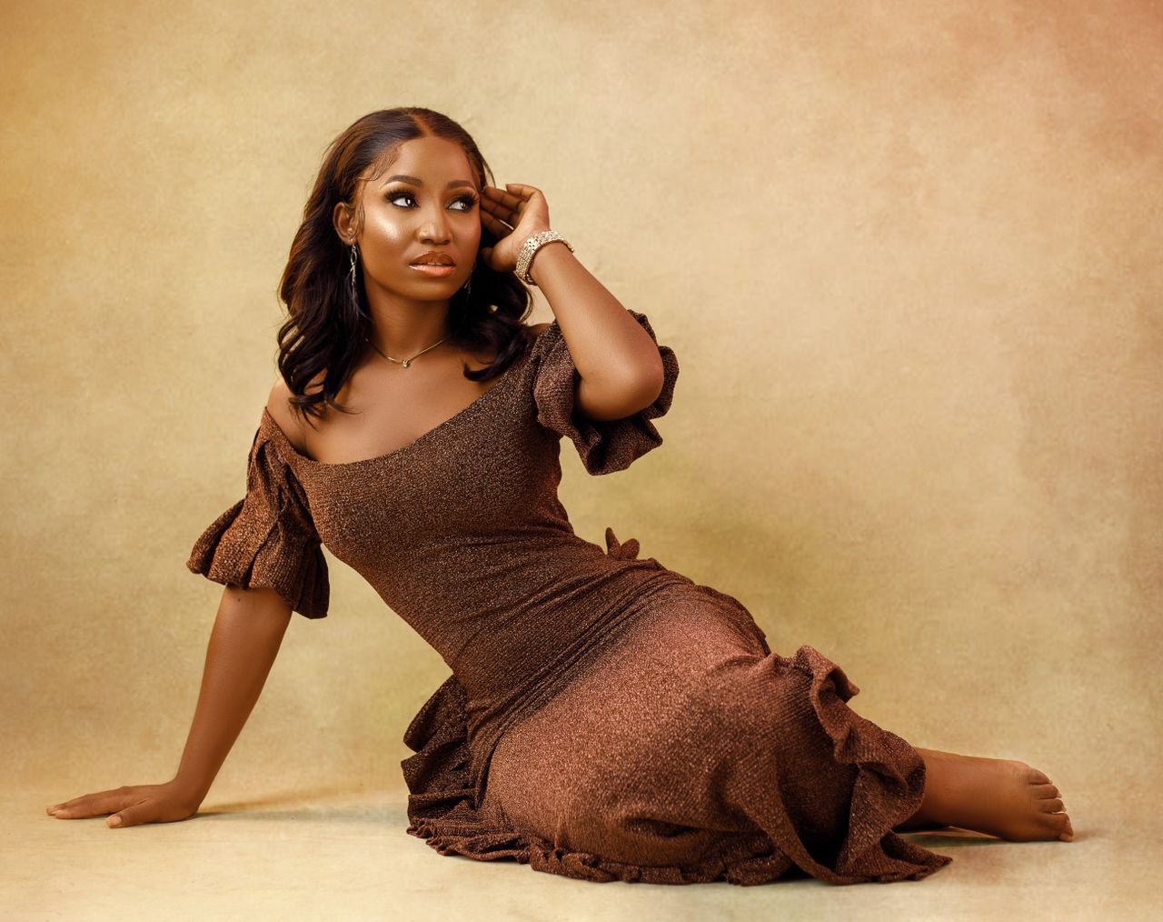A fashionable woman posing elegantly in a brown dress against a yellow gradient background.