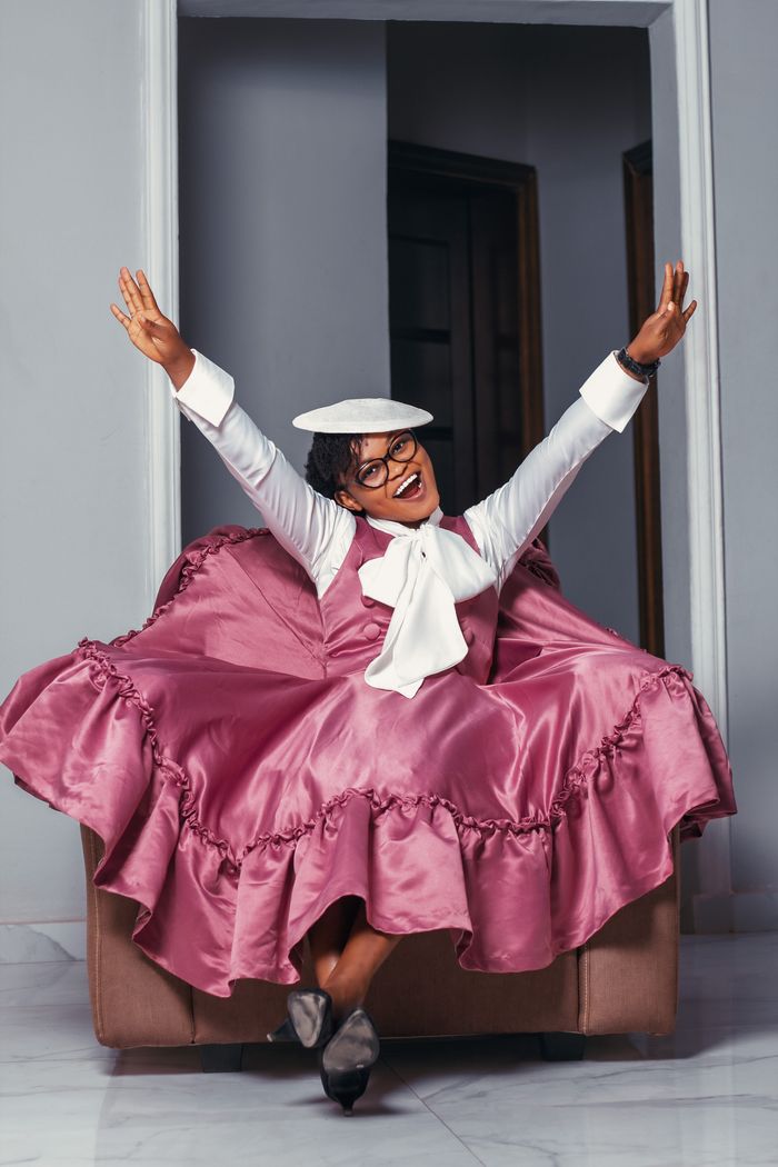 A joyful African woman in a vibrant pink dress celebrates indoors with arms raised.