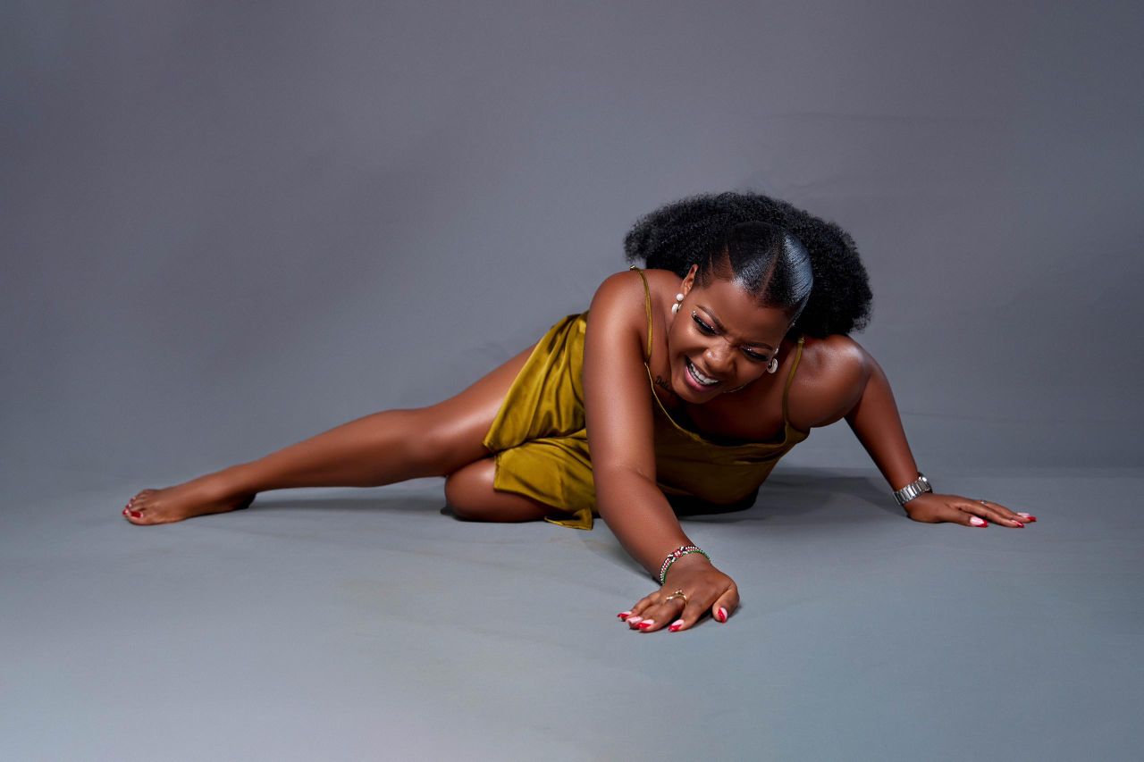 A woman in a yellow dress smiling while lying down in a studio with a gray background.