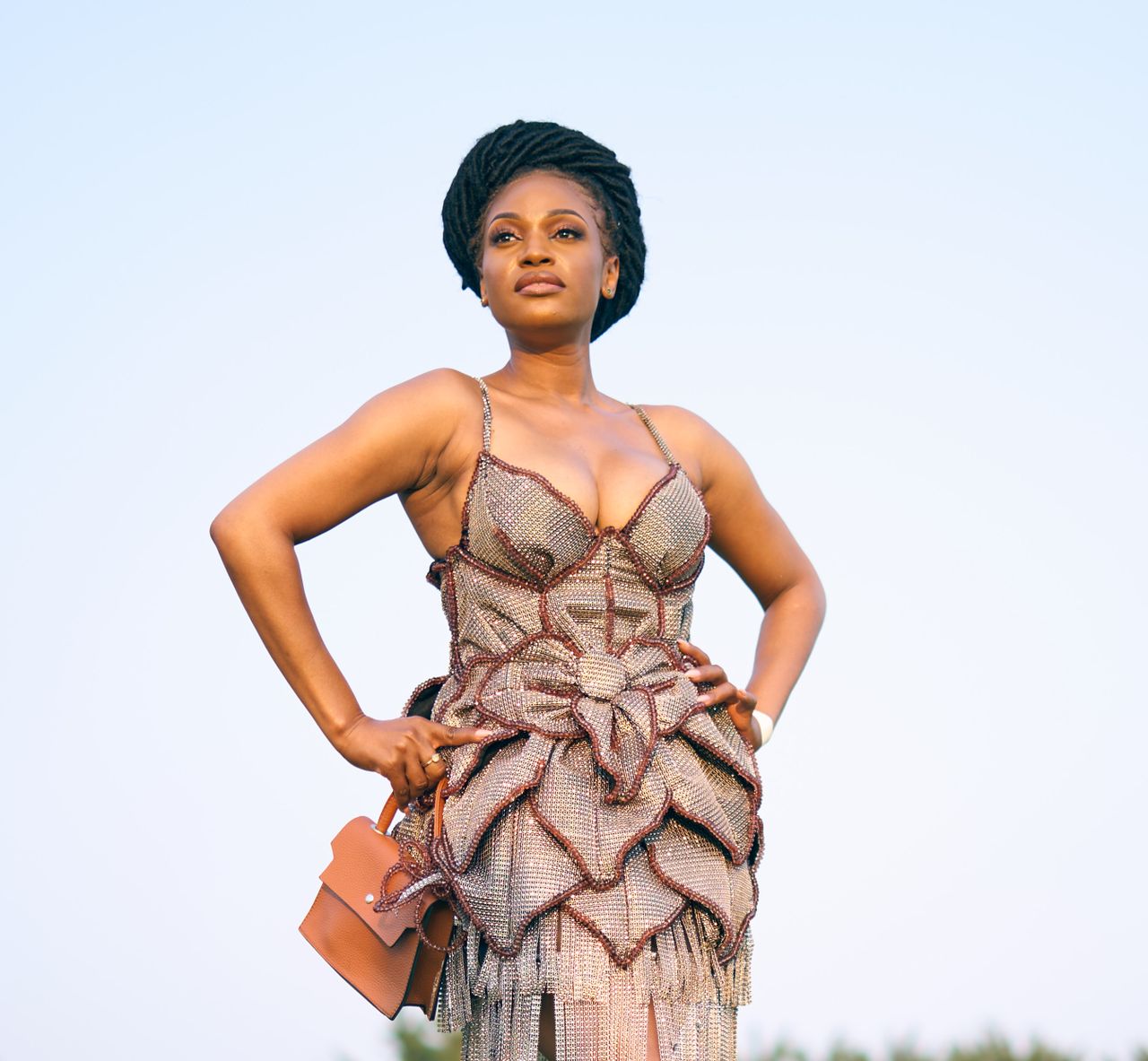 A confident woman poses elegantly in an artistic and stylish dress outdoors.
