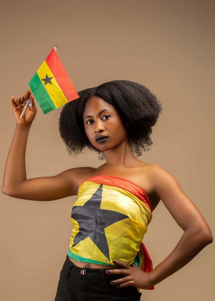 Portrait of woman holding Ghana flag in traditional attire. Celebratory vibe.